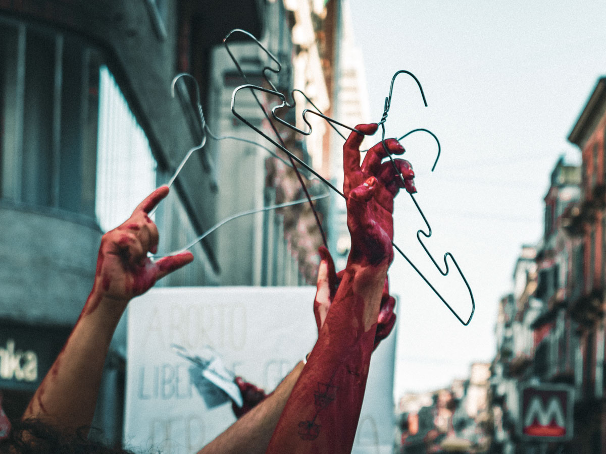 mani, braccia e grucce sporche di vernice rossa si stagliano in cielo durante un coro